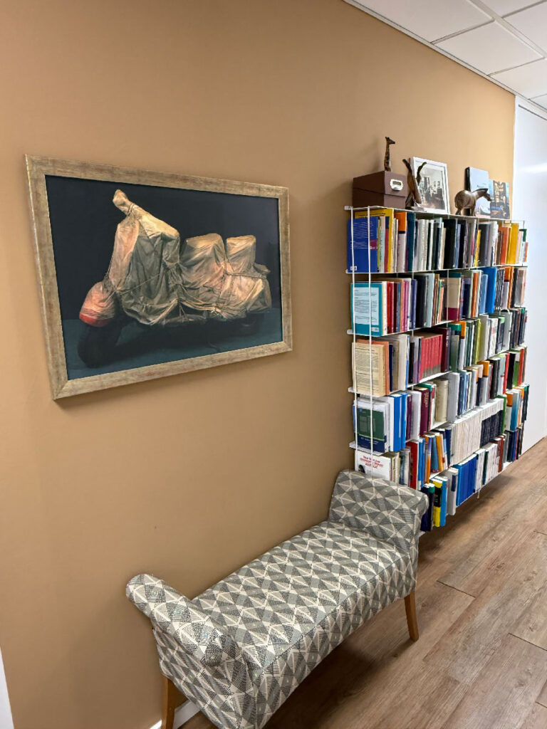 Eine gepolsterte Wartebank, ein gut bestücktes Bücherregal und ein künstlerisch anspruchsvolles Bild an der Wand laden zum Verweilen ein.