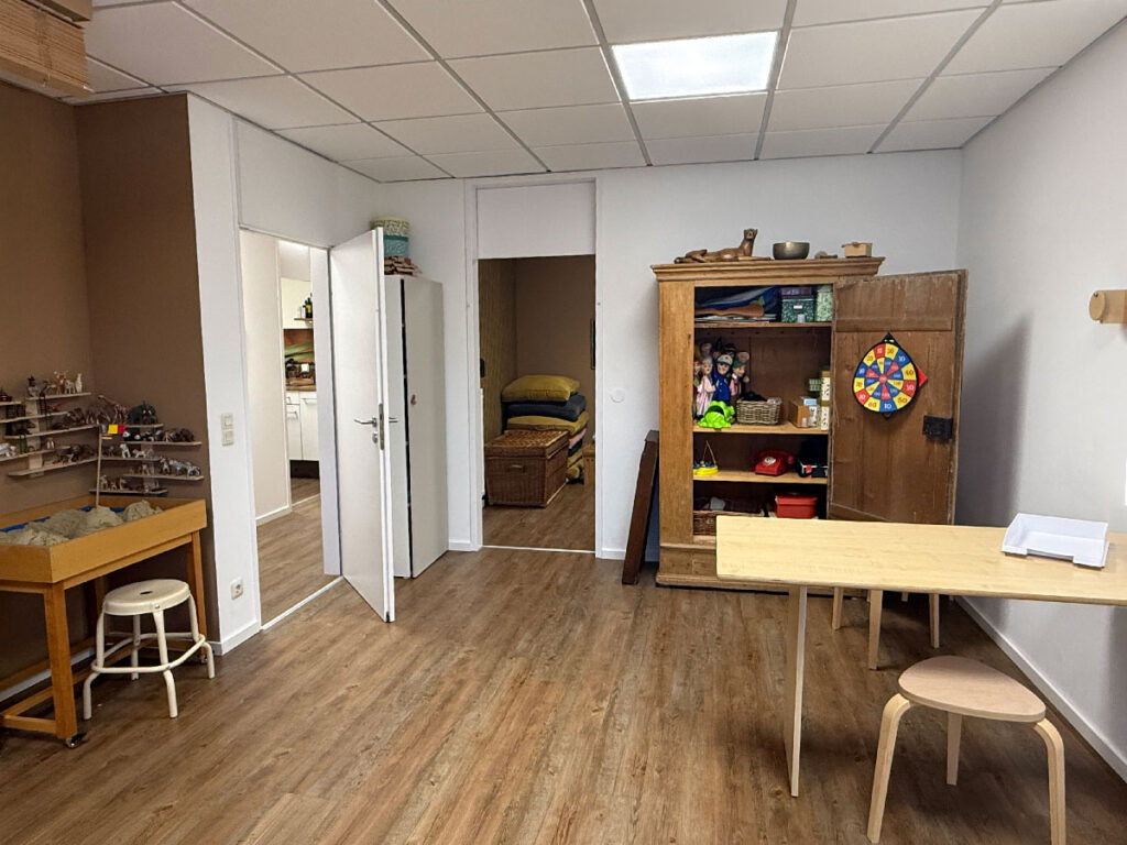 Praxisraum mit offenem Spielschrank, Tisch und Tisch-Sandkasten